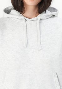 Personne portant un sweat à capuche gris clair avec cordons, se concentrant sur la partie supérieure de la poitrine et du cou, avec des cheveux bruns visibles.