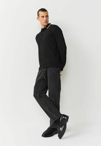 Black long-sleeve polo with a collar, paired with dark gray jeans and black shoes, featuring a minimalist design and no visible patterns.