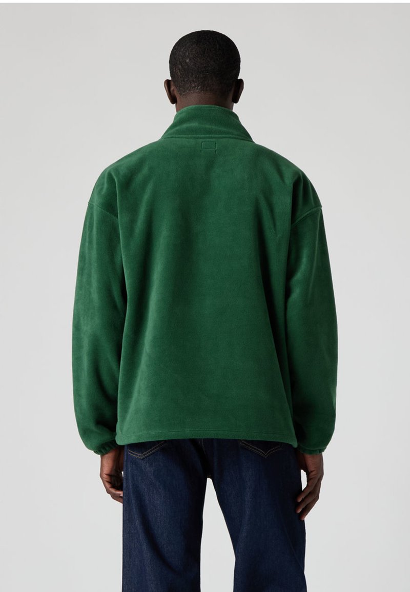 Grön fleecetröja med hög krage, avslappnad passform och mjuk textur. Har en enkel design utan synliga mönster eller metalldetaljer.