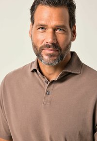 Hnědý bavlněný polo tričko s límečkem, vybavené dvěma tmavými knoflíky a strukturovaným povrchem. Jednoduchý, klasický design s volným střihem.