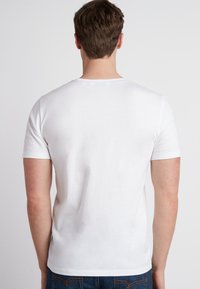 Hvid kortærmet t-shirt lavet af blødt stof. Har en klassisk rund halsudskæring og et enkelt design uden mønstre eller detaljer.