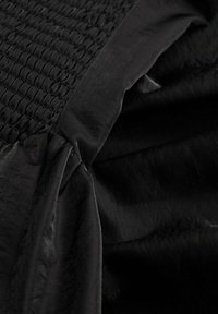 Tissu noir avec un détail de smocks texturé, drapé doux et surface lisse. Présente des nuances variées et un éclat subtil par endroits.