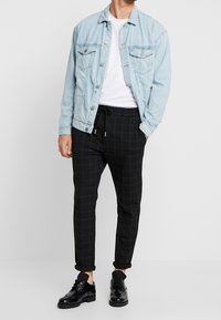 Ljusblå denimjacka över en vit t-shirt, kombinerat med svarta rutiga byxor och svarta skor. Outfiten har en avslappnad passform och upprullade byxben.