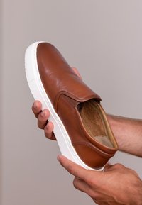 Braune Leder Schlupfschuhe mit einer weißen Gummisohle und glatter Oberfläche. Runde Spitze, ohne Schnürsenkel, mit sichtbarem Innenfutter.