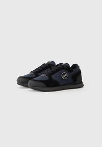 Black and navy sneakers featuring a mix of smooth fabric and suede, rounded toe, laces, and a circular logo on the side.
