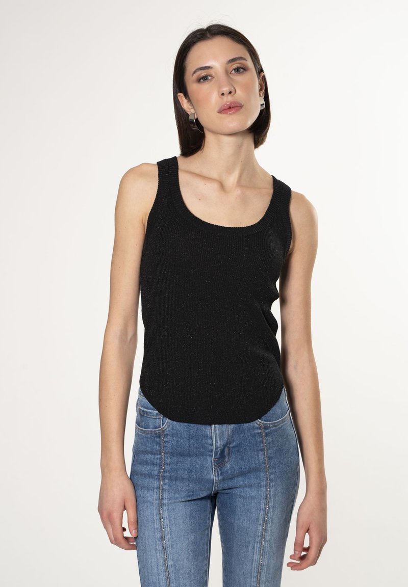 Canottiera nera a coste con scollatura rotonda, realizzata in un filato testurizzato, abbinata a jeans aderenti blu chiaro. L'outfit presenta uno stile casual.