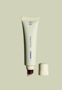 KORRES True Lip Shine en un tubo de color crema, con una tapa de rosca, con una punta cónica y producto burdeos visible.