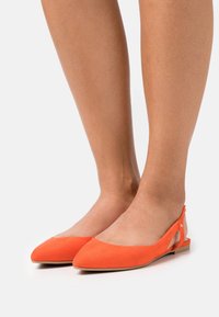 Legs wearing bright orange pointed-toe slingback flats with low heels on a white background.