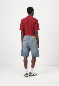 Red ribbed polo shirt, blue denim shorts, white socks, and black sneakers. Shorts have a relaxed fit, 5-pocket design, and a label on the back.