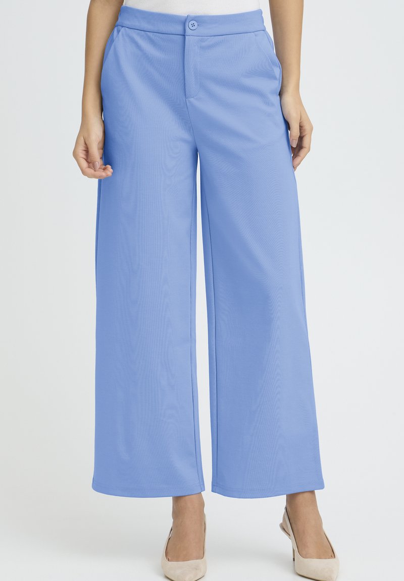 Svetlo modre široke hlače z gladko teksturo, z zapiranjem na gumb in stranskimi žepi, kombinirane s pristnim zgornjim delom in bež petami.