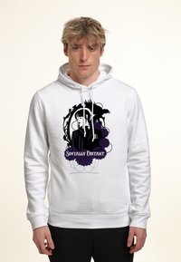 Giovane uomo che indossa un hoodie bianco con una grafica nera e viola di una donna, un corvo, fiori e il testo "Socialmente Distanziato" sul davanti.
