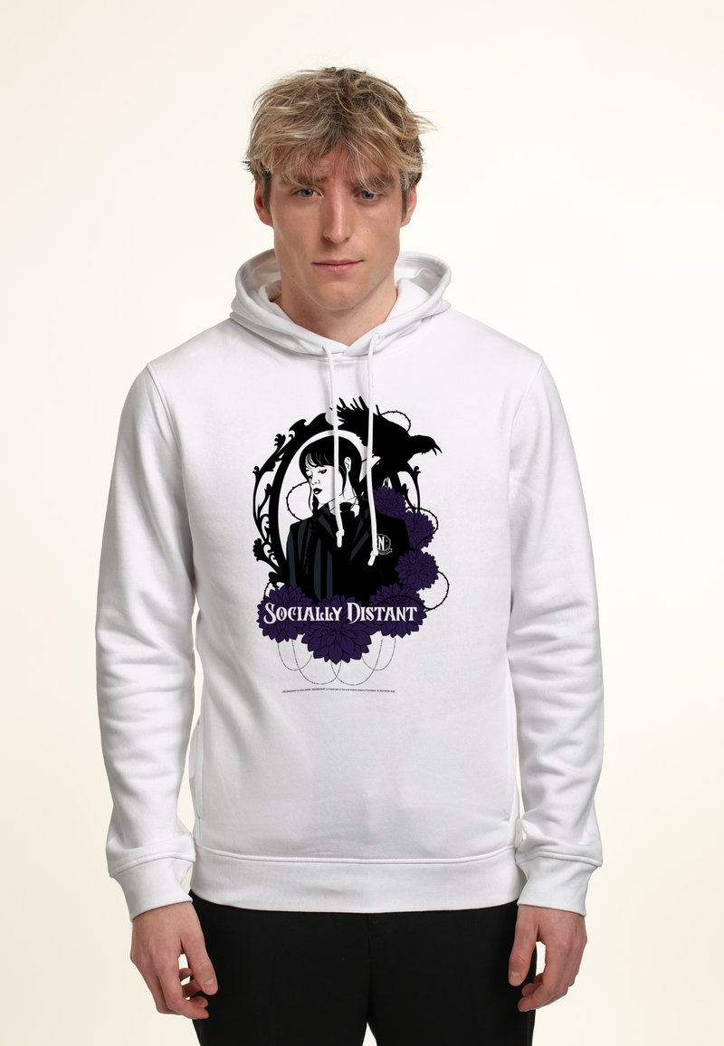 Junger Mann trägt einen weißen Hoodie mit einem schwarzen und lila Grafikmotiv einer Frau, einem Raben, Blumen und dem Text "Sozial distanziert" auf der Vorderseite.