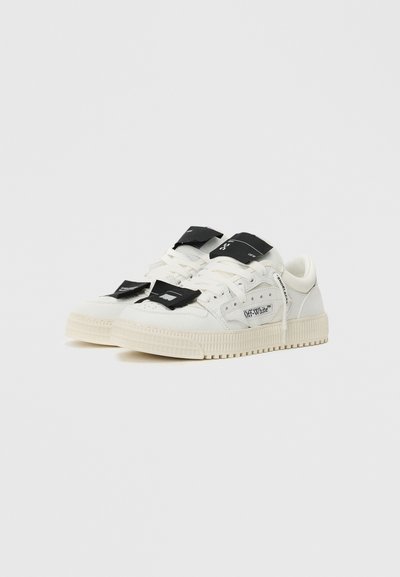 Białe sneakersy z teksturowaną gumową podeszwą, sznurowanym designem i czarnymi metkami z logo na języku. Posiadają perforowane detale po bokach.