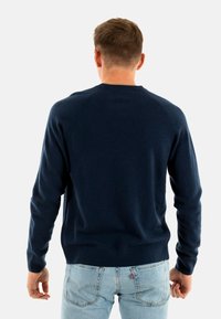 Maglione lavorato a maglia di colore blu navy, con scollatura rotonda e maniche lunghe. Polsini e orlo a costine, caratterizzato da una texture liscia e un design aderente.
