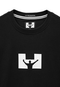 Schwarzes Baumwoll-T-Shirt mit einem weißen Grafikdesign einer Figur mit erhobenen Armen in einem rechteckigen Umriss. Rippenkragen mit einem Etikett.