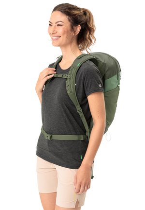Mochila de senderismo verde con correas ajustables, un panel trasero de malla para ventilación y un sistema de hebillas. Lleva puesta una persona con una camiseta oscura.