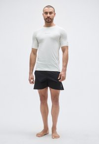 T-shirt de sport gris clair à manches courtes avec un col rond et un logo noir, associé à une jupe de sport noire à ourlet incurvé.