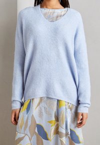 Jasnoniebieski sweter dzianinowy z dekoltem w serek i luźnym krojem, w połączeniu z spódnicą w wielokolorowy wzór kwiatowy z miękkich tkanin.