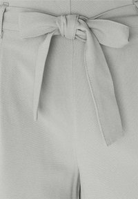 Midjanområdet av ljusfärgade tygbyxor med ett knytet bälte och synliga söm-detajer.