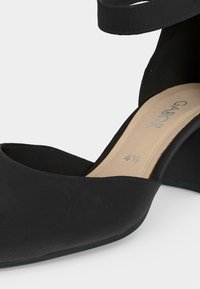 Chaussure noire pour femme à talon bloc avec bride à la cheville, bout pointu et semelle intérieure beige indiquant la pointure 4,5 et la marque Gabor.