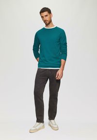 Turkusowa koszula z długim rękawem, z białym dekoltem typu crew neck pod spodem, w połączeniu z ciemnoszarymi spodniami i białymi sneakersami. Gładka faktura i dopasowany krój.