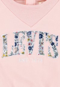 Roza bombažna oblačila z cvetličnim vezenim logotipom "LEVI'S" s belim obodom in "EST. 1873" spodaj v beli niti na teksturiranem ovratniku.