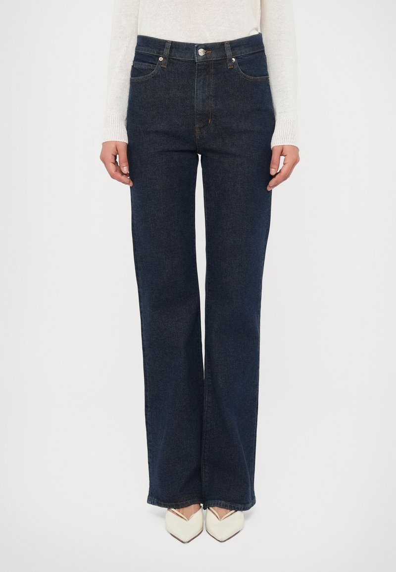 Σκούρο μπλε τζιν με άνετη εφαρμογή, πέντε τσέπες �και φερμουάρ· συνδυασμένο με παπούτσια σε κρεμ απόχρωση με μυτερή μύτη.