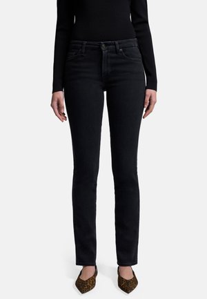 Jean en denim noir à coupe slim, avec une taille mi-haute, des poches avant et un léger délavage. Associés à des chaussures à bouts pointus à motifs.