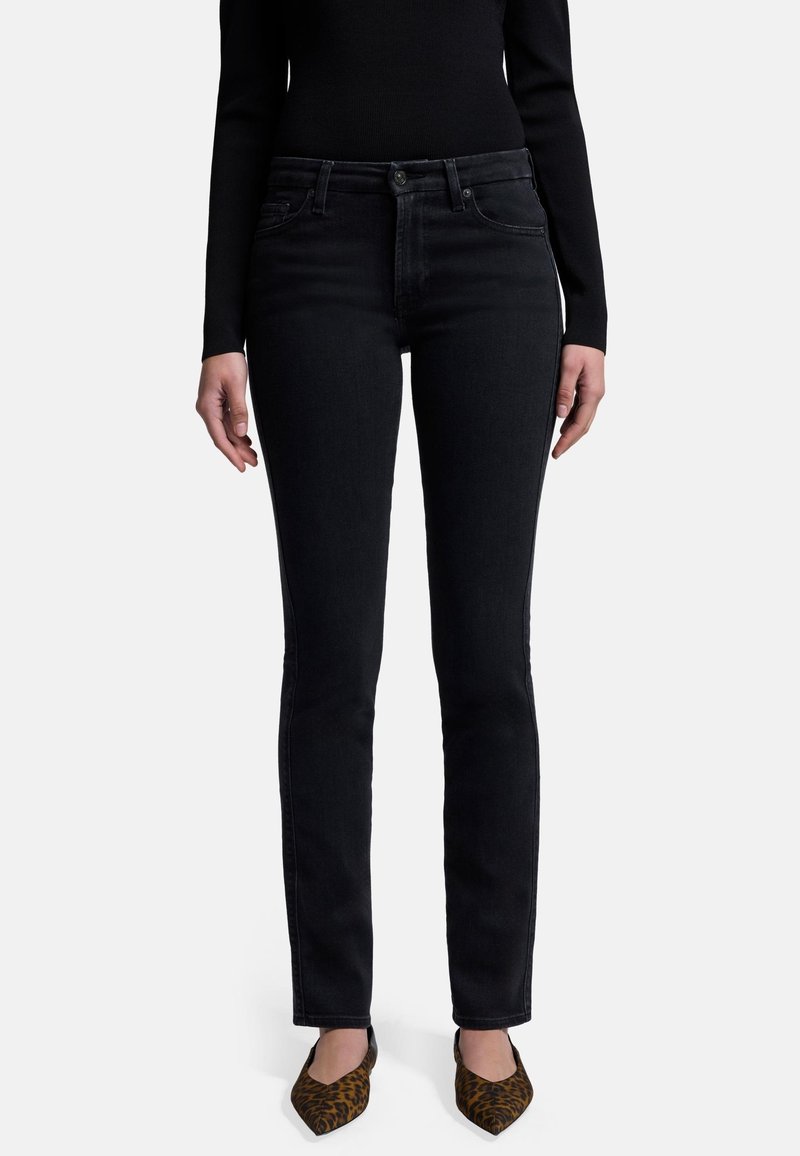 Schwarze Jeans im Slim-Fit mit mittelhoher Taille, Fronttaschen und subtilen Abnutzungen. Kombiniert mit gemusterten, spitz zulaufenden Schuhen.