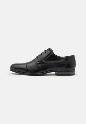 Zapato de cuero negro con punta redonda, diseño con cordones y textura suave. Presenta una marca en el lateral y un tacón bajo apilado.