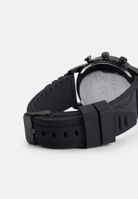 Melna gumijas josta ar nerūsējošā tērauda korpusu, apaļa sejas forma, trīs pogas un gluda, teksturēta apakšpuse.