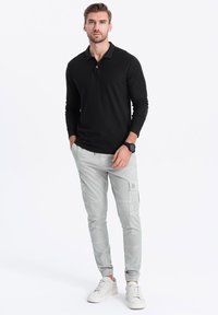 Musta pitkähiha polo-paita yhdistettynä vaaleanharmaisiin cargo-housuihin, joissa on taskut ja joustavat hihansuut, täydentäen asua valkoiset tennarit.