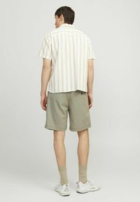 Chemise à manches courtes rayée en blanc avec des lignes pastel, assortie à un short vert. Des baskets blanches et des chaussettes beiges complètent la tenue.