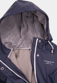 Navy blue waterproof jacket with a soft gray fleece lining, adjustable hood, and zipper closure. Features logo detail and contrasting white trim.