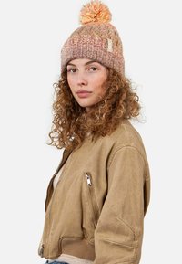 Knit beanie in pink and peach hues, featuring a textured design and a pom-pom on top. Worn with a beige bomber jacket.