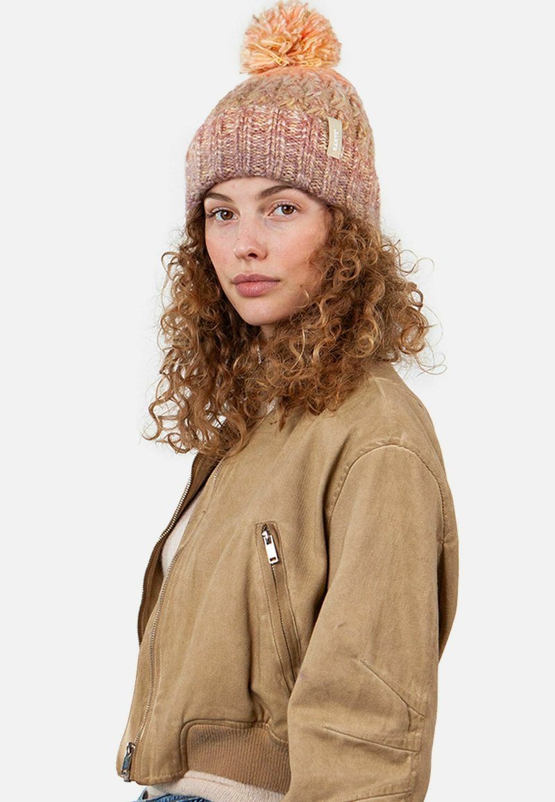 Knit beanie in pink and peach hues, featuring a textured design and a pom-pom on top. Worn with a beige bomber jacket.
