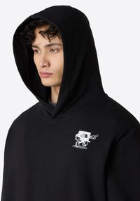 Černá mikina s kapucí, měkký materiál a velká kapuce. Má bílé logo na levé části hrudi.