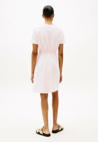 Roze katoenen jurk met korte mouwen, geplooide taille en een rechte zoom. Draag hem met platte, lichtgekleurde sandalen.