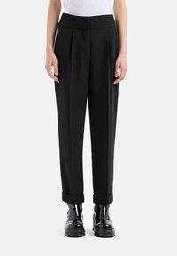 Pantaloni neri sartoriali con vita alta, pieghe e orli arrotolati, realizzati in un tessuto liscio. Abbinati a scarpe nere lucide.