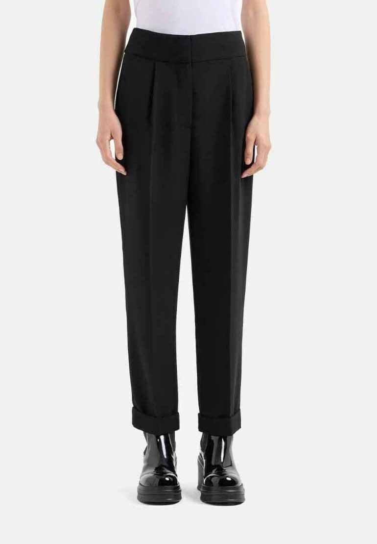 Pantaloni neri sartoriali con vita alta, pieghe e orli arrotolati, realizzati in un tessuto liscio. Abbinati a scarpe nere lucide.