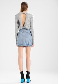 Haut gris à manches longues avec une découpe dans le dos, associé à une jupe en denim clair avec des accents tressés et des bottines noires avec des talons bleus.