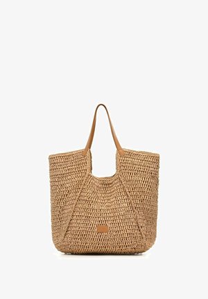 Tkany słomiany worek typu tote z rączkami z jasnobrązowej skóry i małą prostokątną skórzaną naszywką z logo na dole na środku.