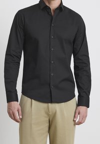 Zwarte longsleeve shirt met een button-down kraag, gemaakt van gladde stof, met een getailleerd ontwerp en subtiele glans. Voorzien van zichtbare knopen aan de voorkant en manchet.