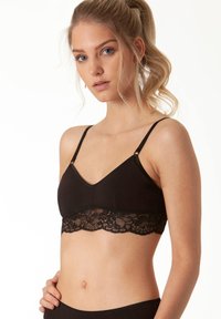 Bralette nera con bordo in pizzo nella parte inferiore, dotata di bretelle regolabili e un tessuto morbido e liscio. Design a scollo a V con una forma strutturata.