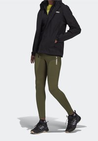 Svart vattentät jacka över gröna leggings, svarta träningsskor med bra grepp och en slimmad passform. Har logotypdetaljer på jackan och leggingsen.