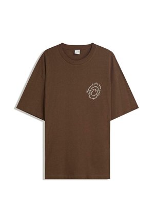 Brązowa bawełniana koszulka z luźnym krojem, krótkimi rękawami i okrągłą białą grafiką na klatce piersiowej. Klasyczny dekolt typu crew neck.