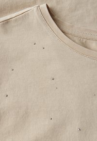 Beige tričko s kulatým výstřihem, na přední straně s rozptýlenými malými stříbrnými ozdobami, vyrobené z jemné bavlněné tkaniny.