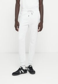 Svetlosivé bavlnené tepláky s elastickým pásom a sťahovacou šnúrkou. Čierne tenisky s bielymi pruhmi a textúrovanou látkou.