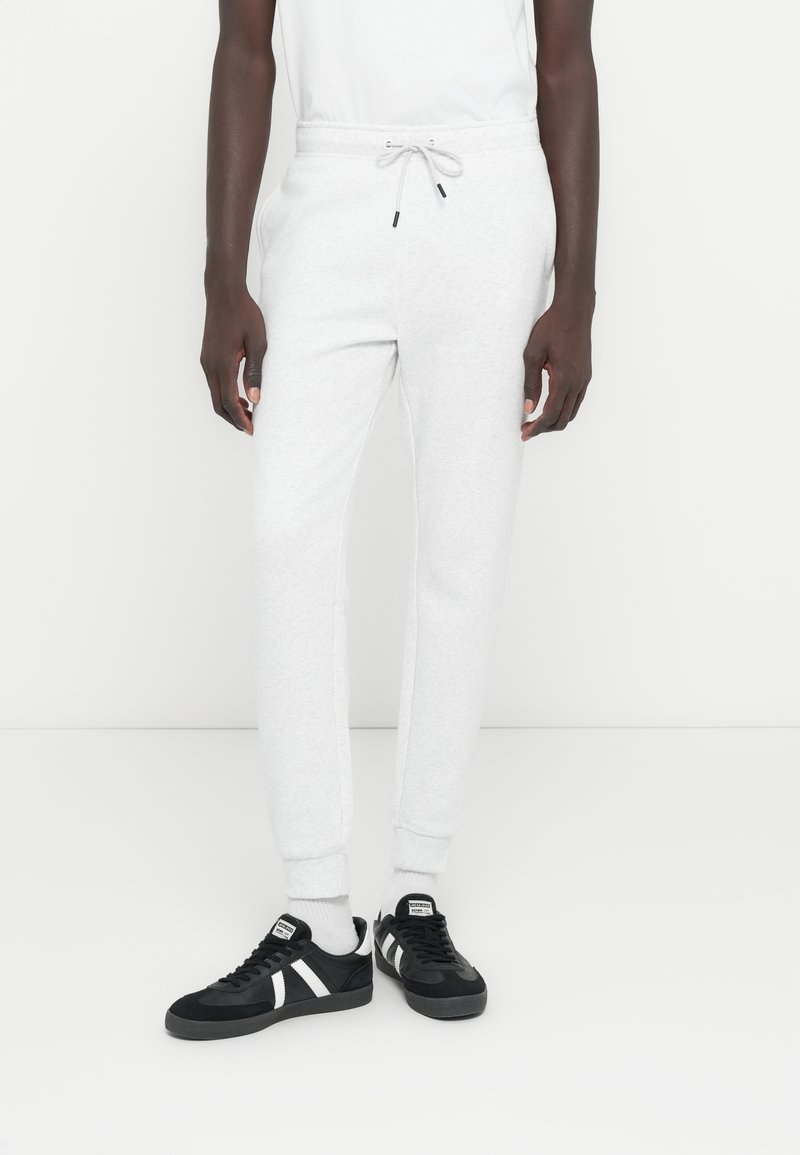 Svetlosivé bavlnené tepláky s elastickým pásom a sťahovacou šnúrkou. Čierne tenisky s bielymi pruhmi a textúrovanou látkou.