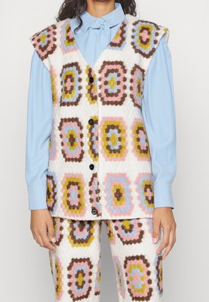 Mouwloze, geknoopte vest en bijpassende broek met kleurrijk geometrisch patroon over lichtblauw overhemd met lange mouwen, vooraanzicht, middenstuk zichtbaar.